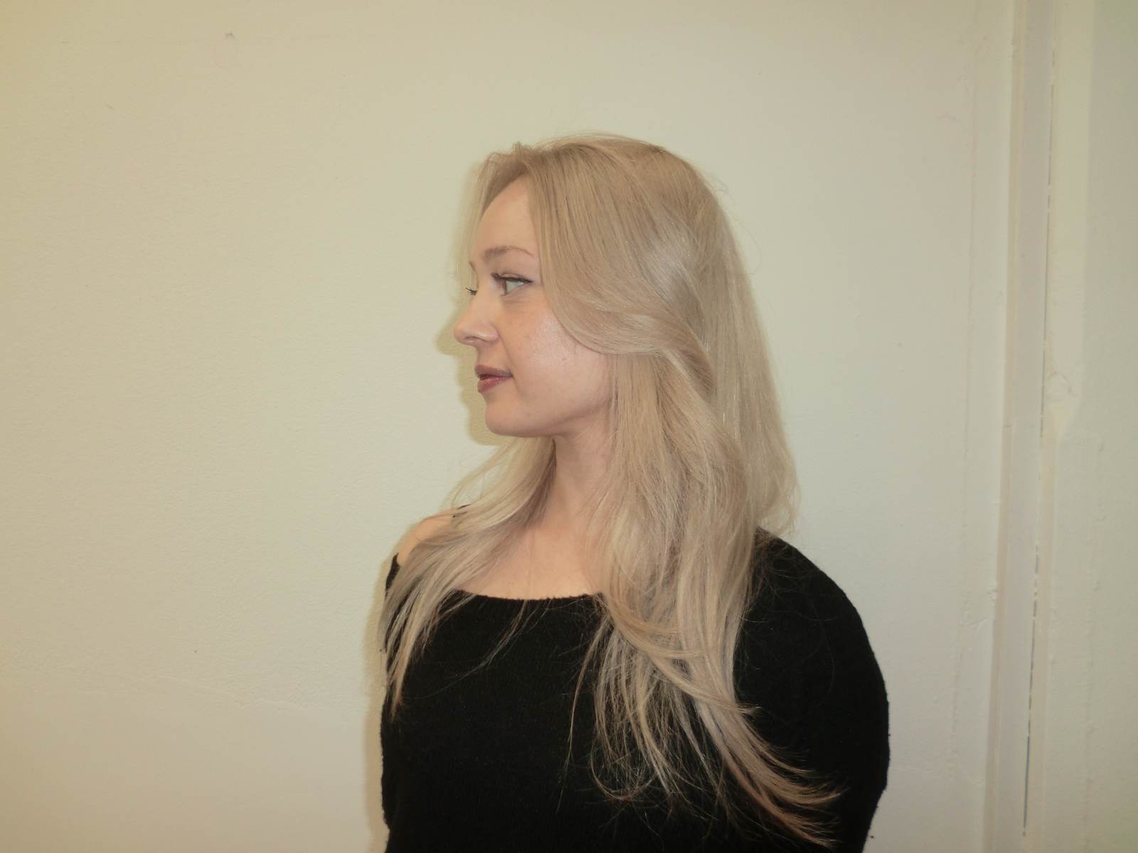 A side profile showing the layered cut of the platinum blonde hair. The long layers curve gently around the face and shoulders, highlighting the uniform, cool-toned color.