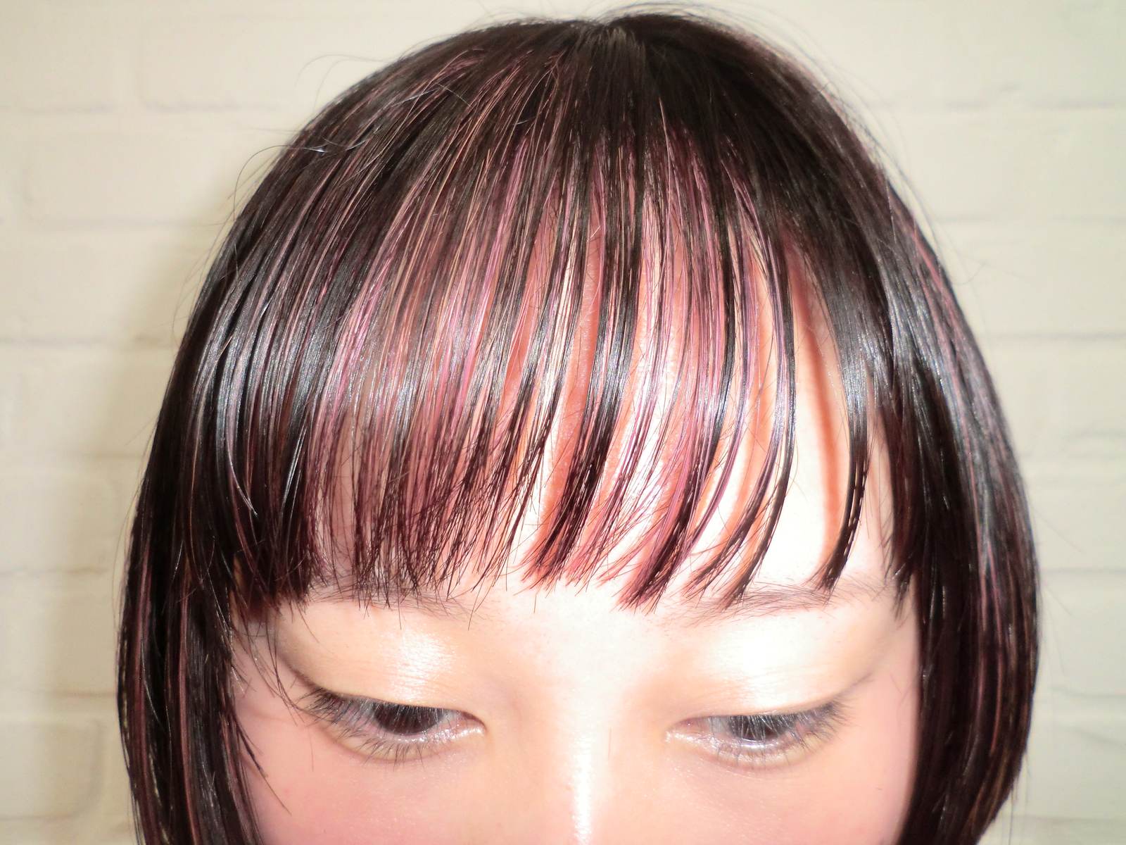 A frontal portrait focusing on textured bangs and face-framing layers. The fringe is a blend of natural black hair and bright pink strands intertwined throughout, creating a multi-dimensional, streaked effect across the forehead.