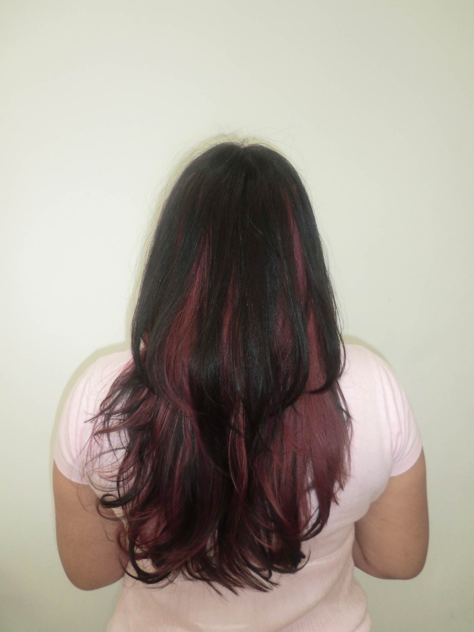 Alt Text: A front profile of a person with long, wavy black hair featuring a high-contrast pink transformation. The full, straight-across bangs are dyed a vibrant magenta pink, which continues into "peekaboo" sections underneath the black top layers. The pink strands frame the face and peek through the dark curls, creating a bold and edgy two-tone look.