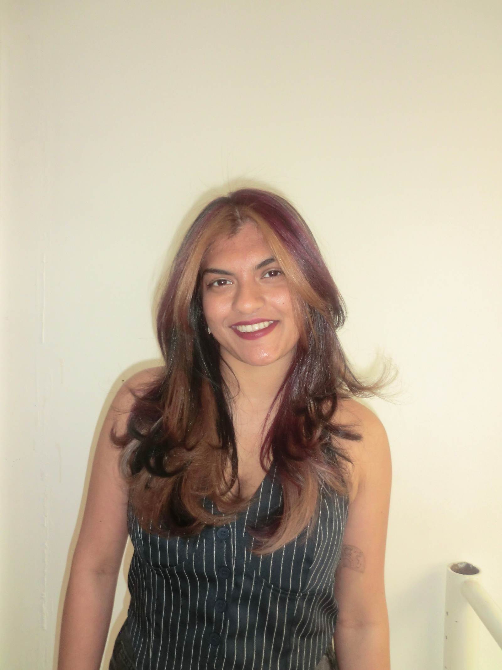 A front profile portrait of a modern "natural calico" hairstyle. The natural black hair base features finely woven, smaller sections of deep mahogany red and warm, bronzy-blonde highlights. This dimensional blend creates a soft, dappled, and high-contrast look that frames the face with rich color without large, blocky sections.