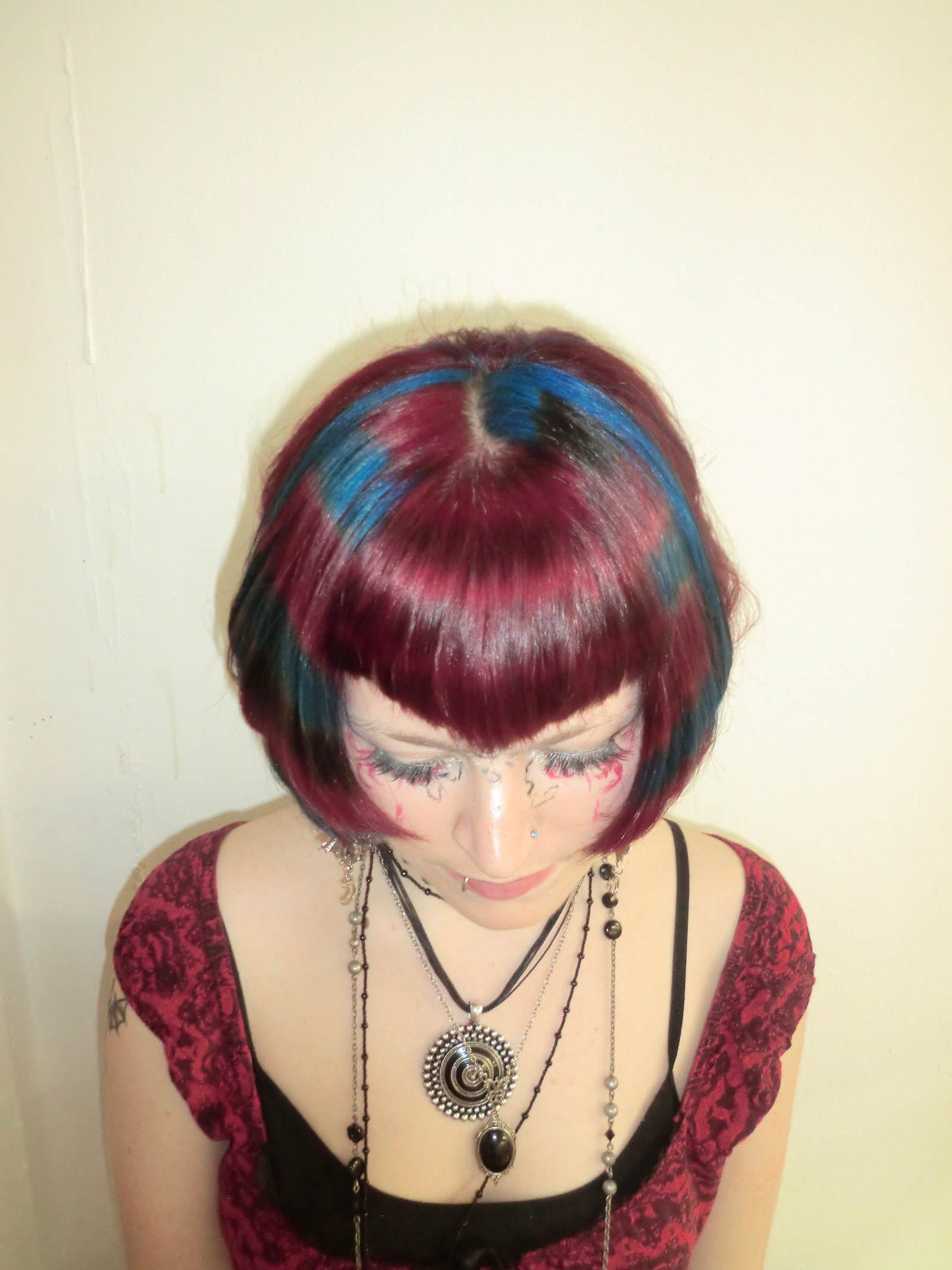 A high-angle front profile showcasing a dramatic creative transformation. The hair is dyed a vivid, all-over crimson red with a sharp V-shaped fringe (v-bangs) at the forehead. The upper angle clearly highlights the precision of the V-cut and the intense saturation of the red pigment at the crown.