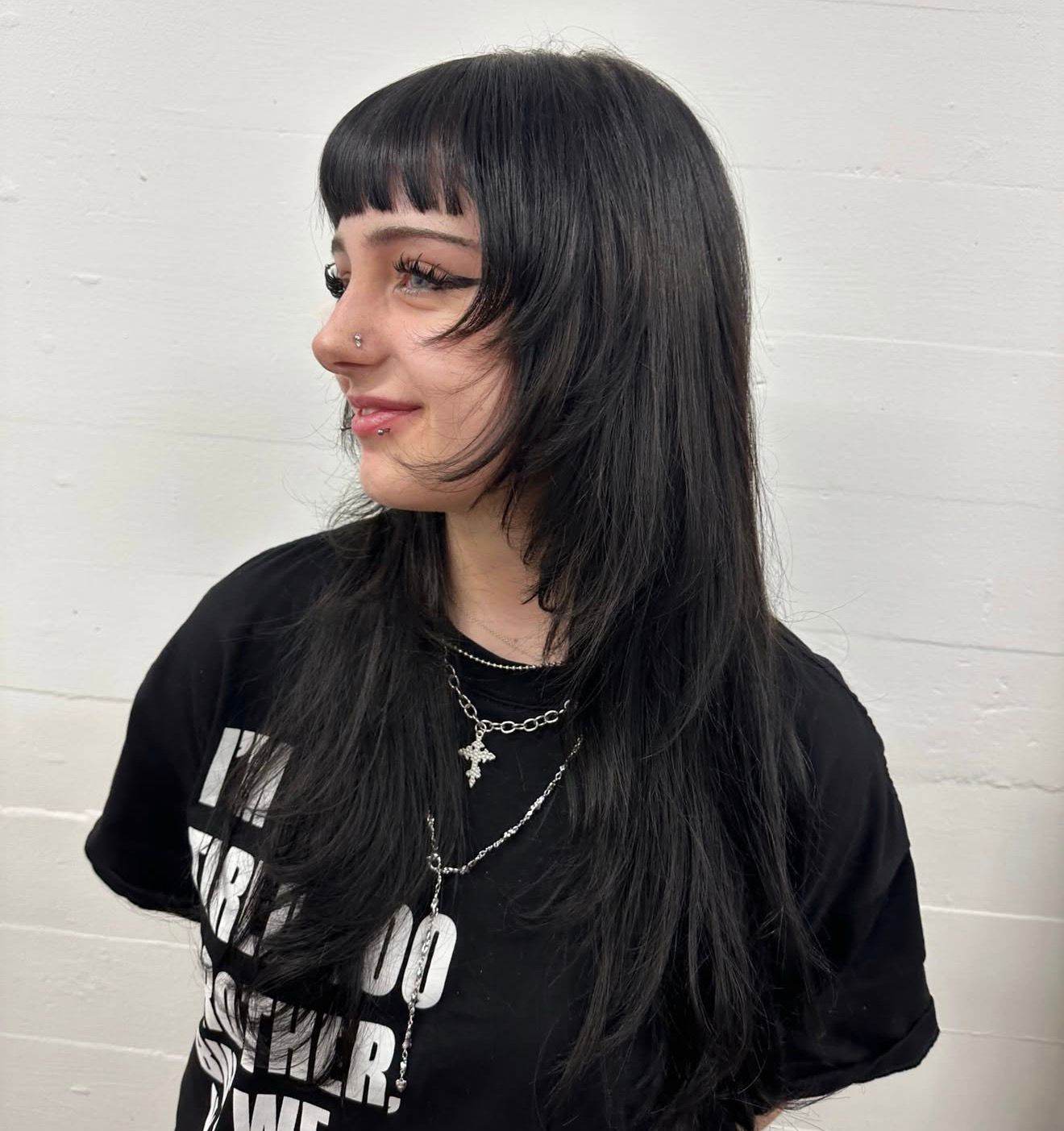 A portrait of a person with long black hair that has been cut into textured layers and styled with voluminous waves. The look features soft, face-framing "curtain" bangs and shorter layers throughout the lengths to add movement and body to the style.