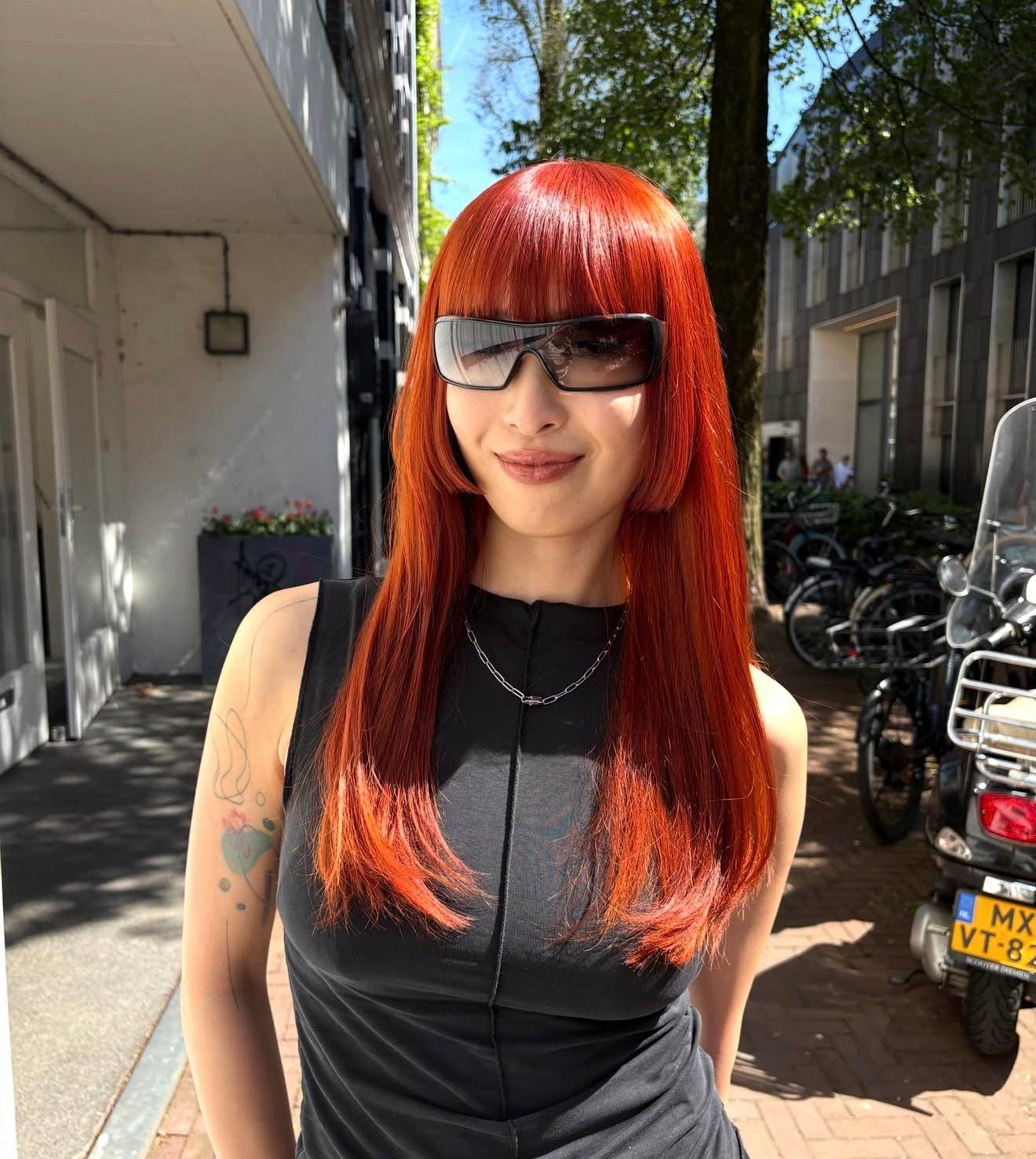 A front profile showcasing a dramatic transformation to a vivid, bright orange hair color. The hair has been reshaped into a structural Hime cut, featuring a thick, straight-across fringe and blunt, cheek-length side-locks that frame the face. The remaining lengths are kept long and straight, highlighting the intense saturation of the copper-orange hue and the sharp geometric lines of the cut.