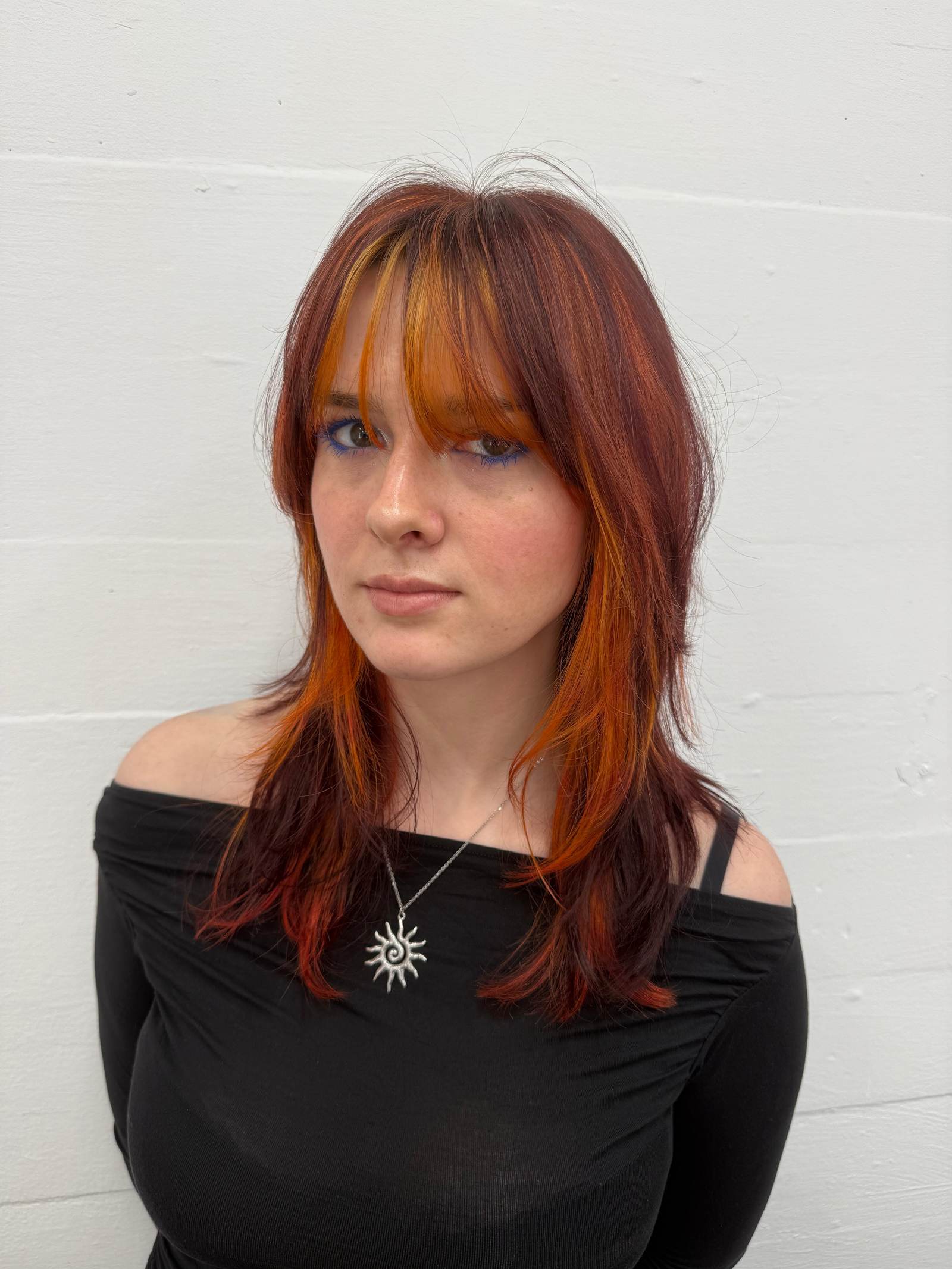 A front profile of a dramatic creative color transformation. The main hair color is a vibrant cherry red, featuring a sharp V-bang fringe with a bright orange peekaboo layer underneath. The face-framing Hime-style layers feature "raccoon tails"—bold, horizontal stripes of orange and red—that contrast against the solid red lengths.