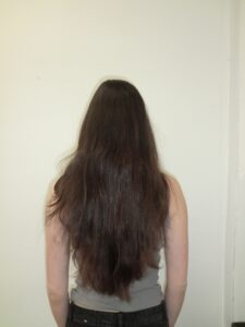 A back view of a person with long, dark espresso-colored hair that tapers into a natural V-shape at the ends. The hair has a subtle, soft wavy texture and appears as a solid, uniform dark tone.