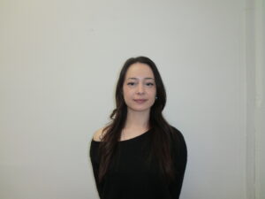 A frontal portrait of a person with long, dark espresso-colored hair. The hair is naturally wavy and styled with a simple side part.