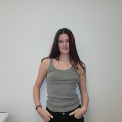 A frontal portrait of a person with long, dark espresso hair featuring vibrant magenta-pink highlights framing the face. The hair is parted in the middle, and the pink "money piece" streaks stand out against the natural dark base