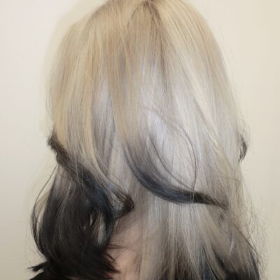 A back view of mid-length hair featuring a high-contrast color design. The top three-quarters of the hair is a bright, icy platinum blonde, while the bottom ends are colored with a deep black "dip dye" effect.