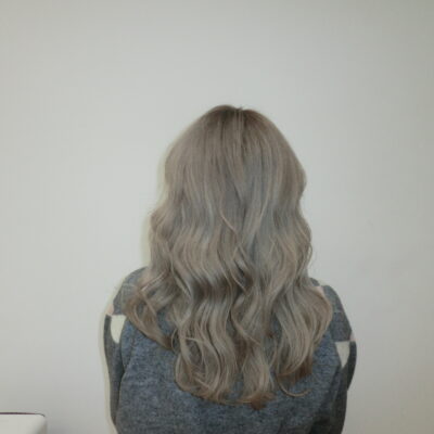 A back view of the same long hair, now transformed into an even, muted "milk tea" or "sesame gray" shade. The color is a sophisticated blend of cool-toned ash and soft charcoal, creating a smoky, translucent finish from roots to ends. The hair is styled with a sleek, straight texture that highlights the multi-dimensional gray tones.
