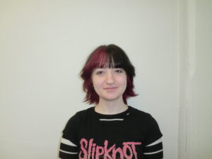 A portrait of a person showcasing a bold color transformation to jet-black hair. The look includes thicker, full bangs with bright red streaks concentrated on the right side, along with a hidden layer of vivid red hair throughout the underneath sections.