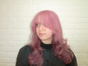 long, vibrant pink hair styled into voluminous "princess curls." The hair falls past the mid-back in thick, uniform ringlets that catch the light, showing various shades of rose and magenta. The curls are bouncy and well-defined, creating a soft, romantic silhouette.