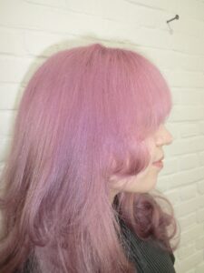 long, vibrant pink hair styled into voluminous "princess curls." The hair falls past the mid-back in thick, uniform ringlets that catch the light, showing various shades of rose and magenta. The curls are bouncy and well-defined, creating a soft, romantic silhouette.