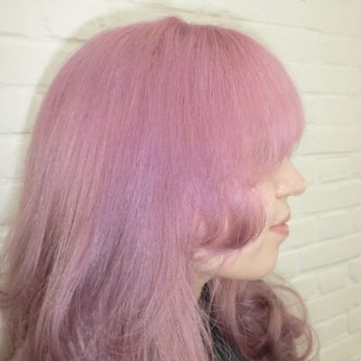 long, vibrant pink hair styled into voluminous "princess curls." The hair falls past the mid-back in thick, uniform ringlets that catch the light, showing various shades of rose and magenta. The curls are bouncy and well-defined, creating a soft, romantic silhouette.