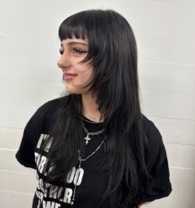 A portrait of a person with long black hair that has been cut into textured layers and styled with voluminous waves. The look features soft, face-framing "curtain" bangs and shorter layers throughout the lengths to add movement and body to the style.