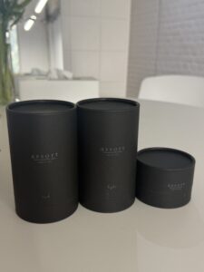 A professional product shot of three Assort hair care items standing side-by-side against a clean background. From left to right: the Assort Multi Balm in a short, wide black matte cylinder jar with a minimalist white label, the Assort Multi Oil Rich in a taller black matte cylinder bottle with a dropper top, and the Assort Multi Oil Light in an identical tall black matte bottle. The heights create a stepped look, with the oils standing taller than the balm.
