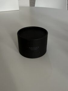 A close-up shot of the Assort Multi Balm in its signature packaging. The product is contained in a short, wide, black matte cylinder jar with a clean white label featuring minimalist black text. Its low-profile shape distinguishes it from the taller oil bottles in the collection.