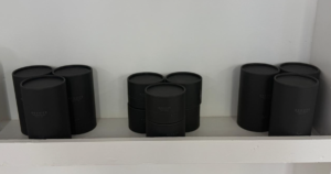 A lifestyle shot of the Assort product line arranged on a sleek salon shelf. The Assort Multi Balm, Multi Oil Rich, and Multi Oil Light are displayed together, showcasing their cohesive black matte cylinder packaging and clean white labels. The two oil bottles stand taller than the balm jar, creating a uniform and premium professional aesthetic.