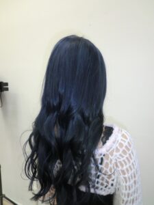 A back view of the same hair, now dyed a deep, saturated dark blue. The color is a consistent midnight navy tone from roots to ends, styled to show off the hair's natural texture and the new cool-toned hue.