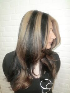 A side profile view showcasing the contrast of skunk highlights. A wide section of bright blonde hair runs vertically from the crown to the ends, sandwiched between layers of natural black hair. The sleek, straight styling emphasizes the clean lines between the two opposing colors.