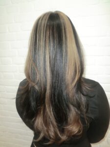 A back view of long black hair with chunky skunk-style highlights. Large, distinct sections of platinum blonde are woven through the dark base, creating a patchwork or "stripe" effect. The contrast is sharp and unblended, showcasing the bold color blocking from behind.