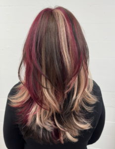A back view of a classic calico color style. The hair is a mix of bold sections in dark red, pale blonde, and deep chocolate brown, blended together to create a high-contrast, multi-tonal look throughout the lengths.