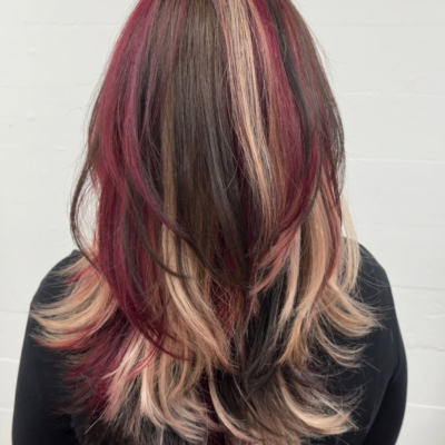 A back view of a classic calico color style. The hair is a mix of bold sections in dark red, pale blonde, and deep chocolate brown, blended together to create a high-contrast, multi-tonal look throughout the lengths.
