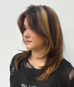 A side profile of a "natural" calico hairstyle. The look features chunky, distinct sections of jet black, chocolate brown, and sandy blonde hair. The placement showcases the high-contrast color blocks as they fall over the shoulder, creating a patchwork effect using a more grounded, neutral color palette.