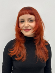 A front profile view of an intense, all-over neon orange hair color. The hue is extremely bright and saturated, and the hair is styled in a simple, sleek middle part, falling to the shoulders.