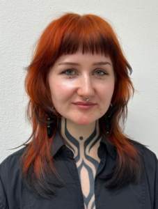 A front profile of vibrant, electric orange hair with a high-contrast finish. The tips of the hair are saturated in deep black color, creating a dramatic black dip dye "fox tip" result against the bright base.