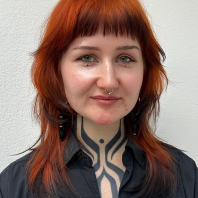 A front profile of vibrant, electric orange hair with a high-contrast finish. The tips of the hair are saturated in deep black color, creating a dramatic black dip dye "fox tip" result against the bright base.