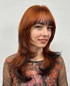 A front profile featuring a muted, dusty orange or copper hair color. The very ends of the hair, including the face-framing pieces, are finished with a stark black dip dye, creating a sharp "fox tip" effect.