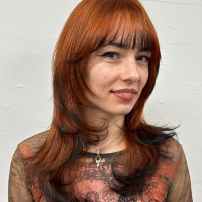 A front profile featuring a muted, dusty orange or copper hair color. The very ends of the hair, including the face-framing pieces, are finished with a stark black dip dye, creating a sharp "fox tip" effect.