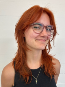 A front profile of vibrant, all-over orange hair. The shade is saturated and even from roots to ends, styled forward and falling just past the shoulders with a straight texture.