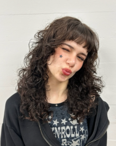 A view of medium-length hair with a tight, natural curly texture. The curls are well-defined and voluminous, showcasing a dark, uniform color with a soft, rounded shape.