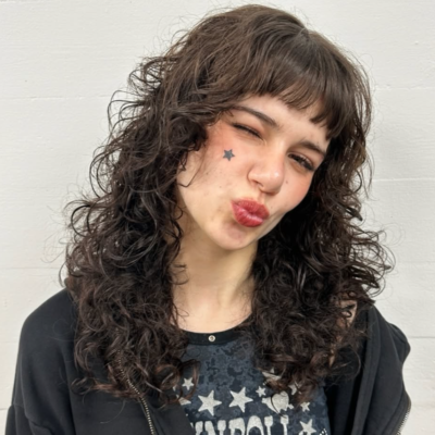 A view of medium-length hair with a tight, natural curly texture. The curls are well-defined and voluminous, showcasing a dark, uniform color with a soft, rounded shape.