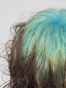 A close-up back view of a short, grown-out bixie cut (a hybrid between a pixie and a bob). The hair is predominantly natural medium brown, but features hidden "ghost roots" in a vibrant teal-mint green hue at the nape of the neck. This peek-a-boo color only becomes visible when the upper, brown layer of hair is slightly lifted or moves.