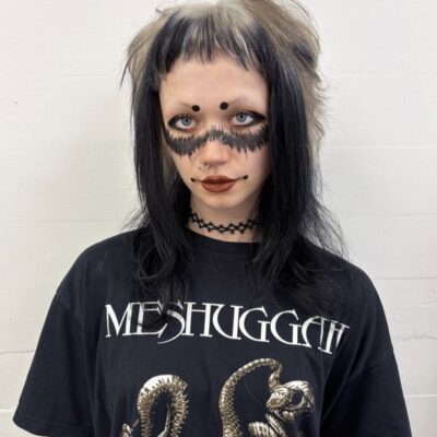 A front profile showcasing an edgy, texturized shaggy haircut. The top and crown sections are a bright, metallic platinum silver that transitions sharply into solid jet-black ends. The thick bangs feature a bold colorblocked design, split vertically into a striking half-silver and half-black pattern that heavily frames the face.