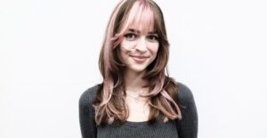 A front profile showing a bold hair transformation. The hair has been cut to chest-length and styled straight. It features large, chunky pink highlights that contrast sharply against a dark brunette base. The pink sections are particularly prominent around the face-framing layers and crown, creating a vibrant, color-blocked aesthetic.