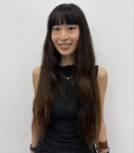 A front profile of a person with very long, solid jet-black hair. The hair is styled simply with a center part, cascading straight past the shoulders with minimal layering and a consistent deep raven tone.