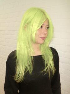 A vibrant after-shot of the complete hair transformation. The roots and lengths have been flawlessly lifted and saturated in a high-visibility, electric neon yellow shade. The color is completely uniform from the scalp to the tips, giving off a bold, glowing, and monochromatic look.