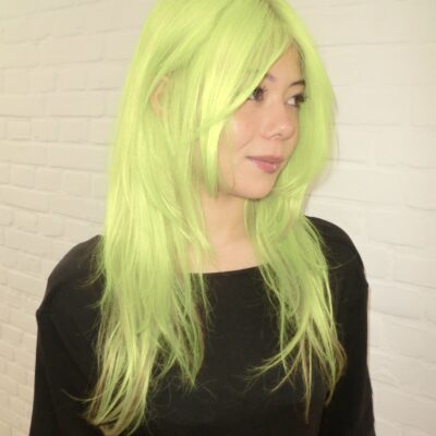 A vibrant after-shot of the complete hair transformation. The roots and lengths have been flawlessly lifted and saturated in a high-visibility, electric neon yellow shade. The color is completely uniform from the scalp to the tips, giving off a bold, glowing, and monochromatic look.