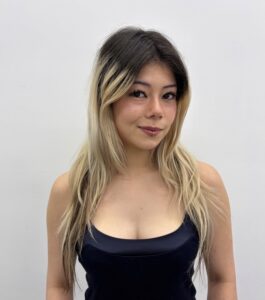 A close-up view of hair before a color treatment, showing several inches of natural jet-black root grow-out. The dark roots contrast sharply against the rest of the length, which is a faded, pale platinum blonde.