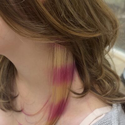 A side profile view showcasing the layered contrast of the new color. The top sections are a bright, multi-tonal blonde, while the exposed under-layer features bold, distinct horizontal stripes of hot pink and platinum blonde stacked vertically to create a sharp raccoon pattern along the side of the head.